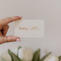 Hand holding a card with 'Avery' printed on it, in front of white tulips.