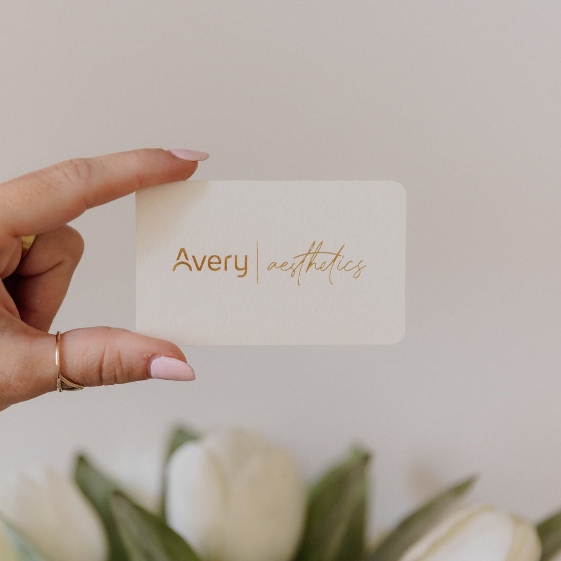 Hand holding a card with 'Avery' printed on it, in front of white tulips.